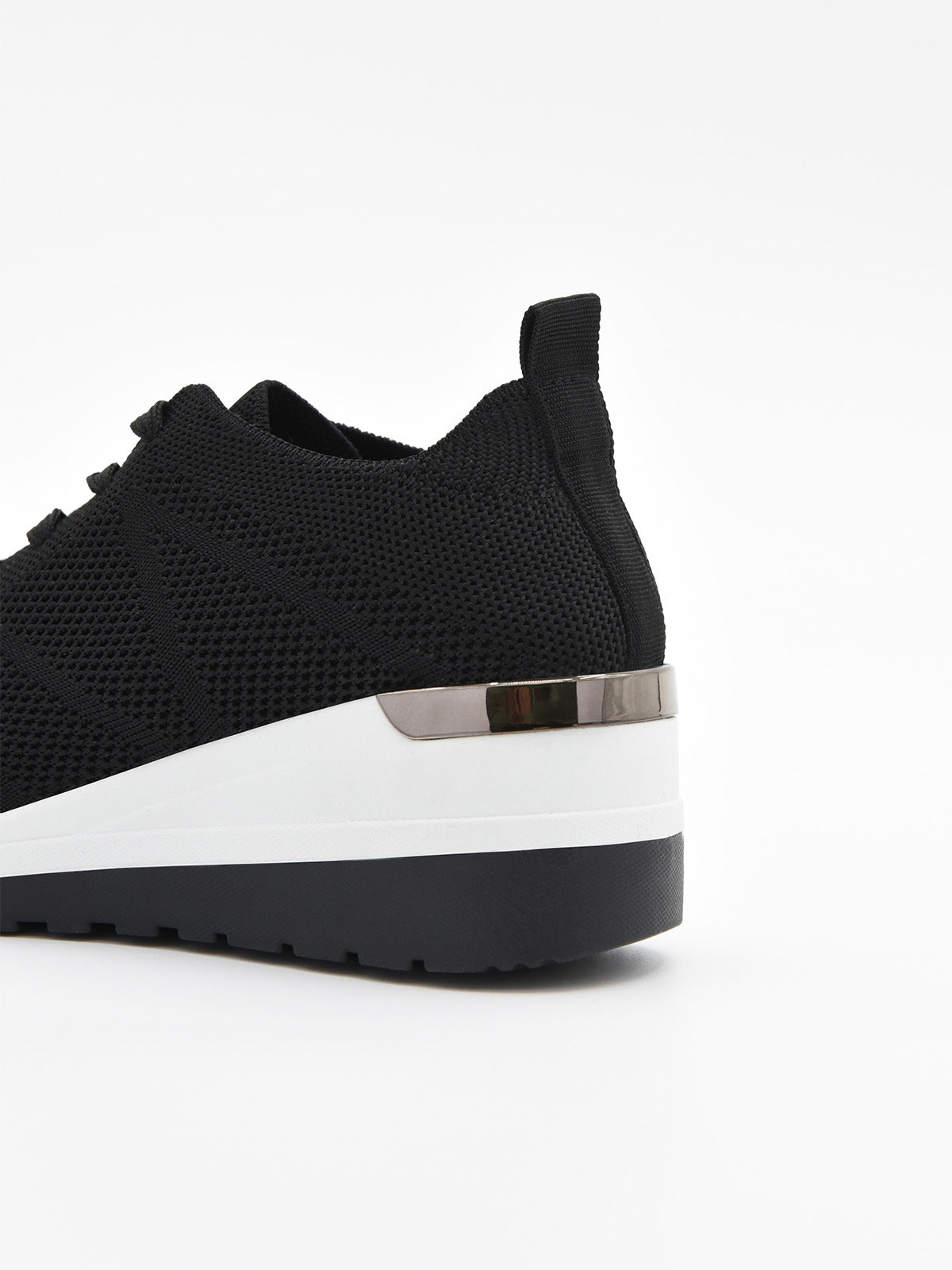 Zapatilla negra de tejido transpirable, con agujetas, plataforma bicolor blanca y negra, y detalle metálico en el talón.
