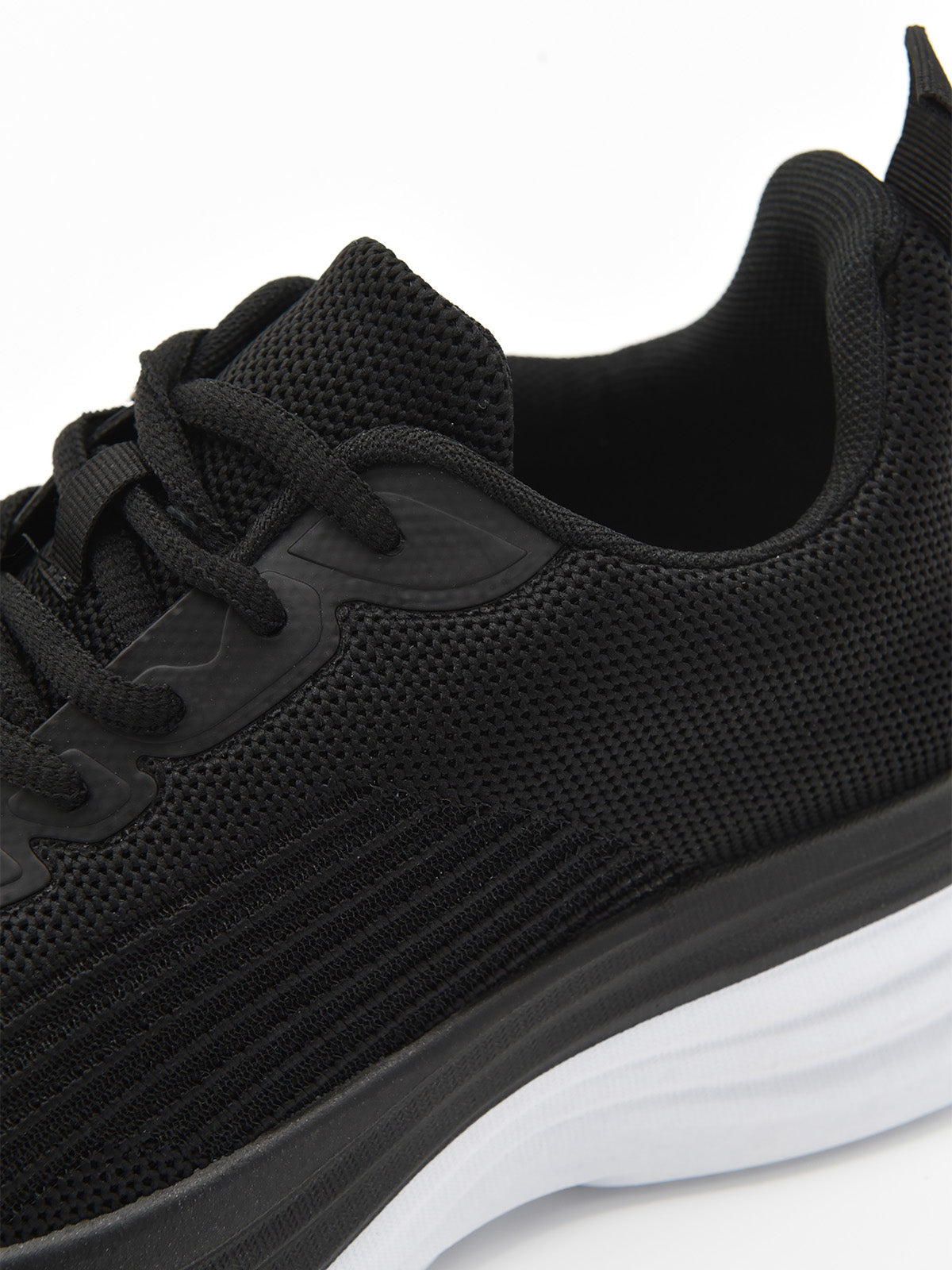 Zapatilla deportiva de tejido negro con cordones, suela gruesa blanca y detalles en negro en la base.
