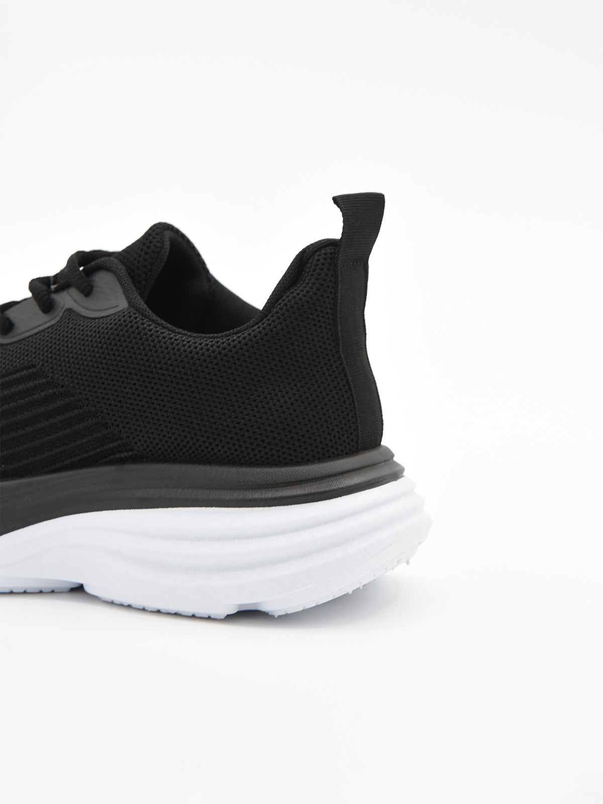 Zapatilla deportiva de tejido negro con cordones, suela gruesa blanca y detalles en negro en la base.