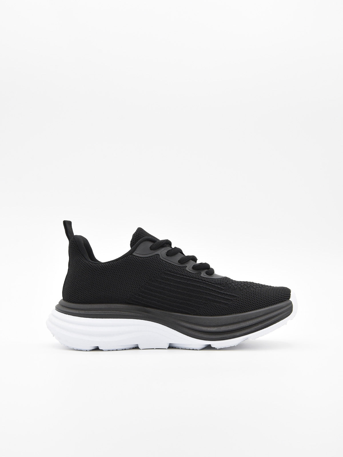 Zapatilla deportiva de tejido negro con cordones, suela gruesa blanca y detalles en negro en la base.