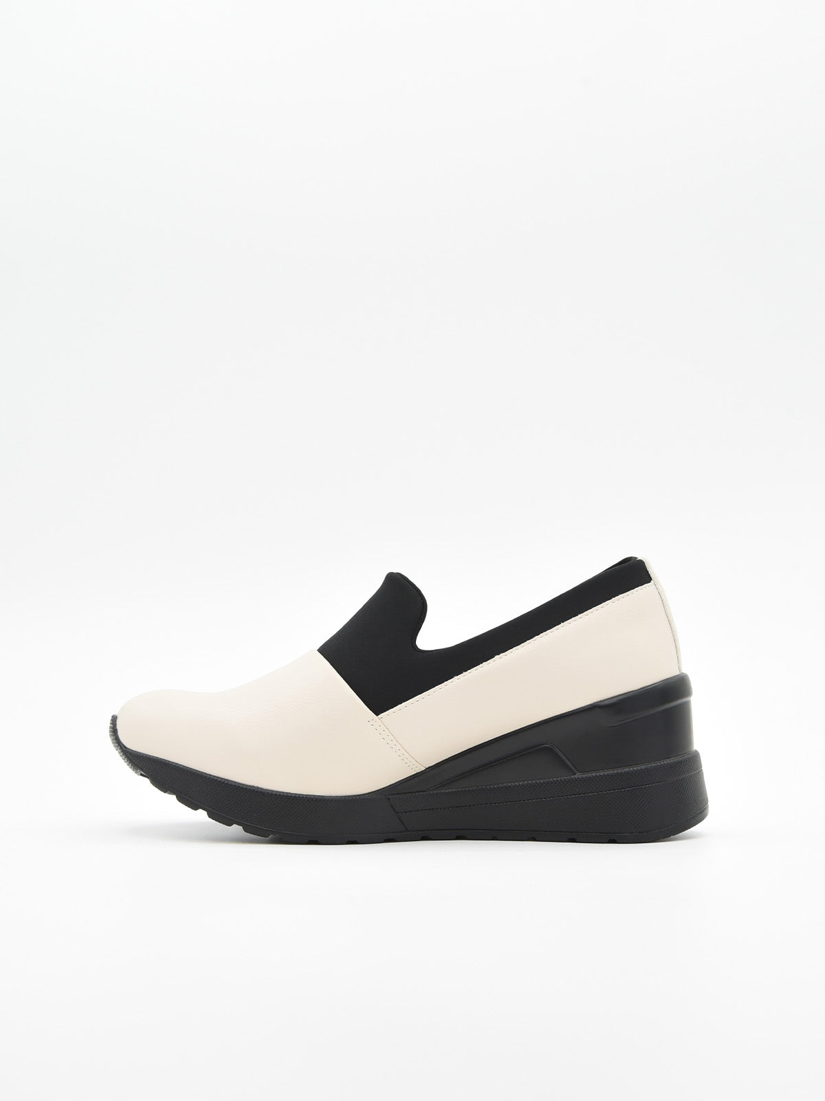 Zapato casual bicolor para mujer, en tonos crema y negro, estilo slip-on con elástico superior y plataforma ergonómica continua.