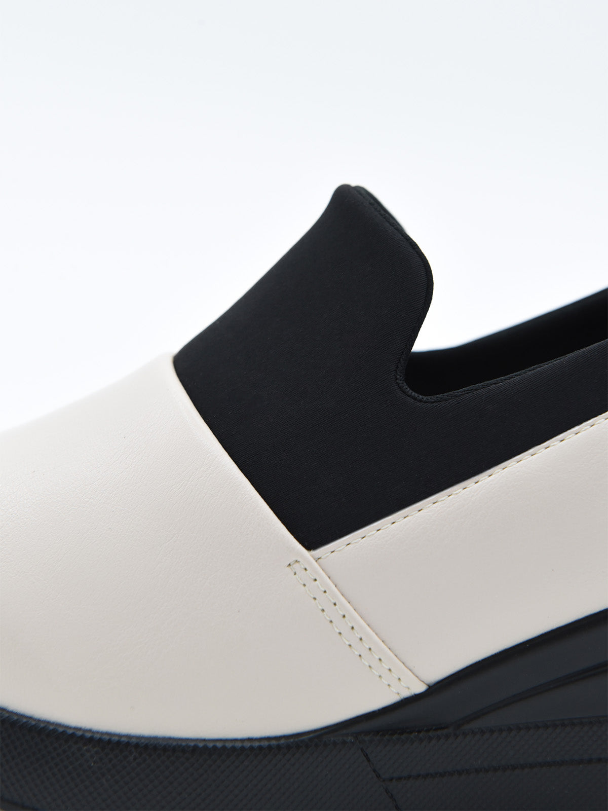 Zapato casual bicolor para mujer, en tonos crema y negro, estilo slip-on con elástico superior y plataforma ergonómica continua.